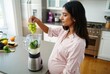 © LIDIIA - Pregnant woman making smoothie. A healthy pregnant woman adds fresh grapes to a blender with spinach to make a nutritious green smoothie.