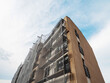 © mark_gusev - Residential apartment building during facade repair or renovation with scaffolding around it in safety mesh. Property upgrade, job increasing value of the home. Construction site.