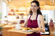 © JackF - Saleswoman walks between tables in a coffee shop and holds a tray of delicious coffee and buns in her hands.