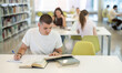 © JackF - Young male student reading book and taking notes sitting at table in library