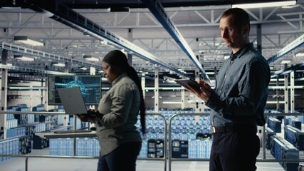 Data center software developers investigate neural networks configuration, making adjustments to ensure optimal function. Server farm workers use tablet to check deep learning error reports, camera A
