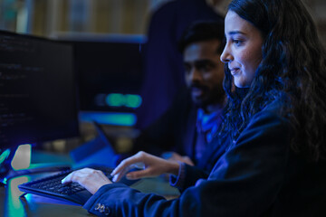 A diverse team of AI developers in a late-night coding session. A senior engineer uses a tablet to guide a programmer as they collaborate on building a complex neural network.