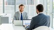 © ng-TDRD - Two professionals engaged in a business discussion, one smiling while the other focuses on a laptop, showcasing a modern office environment.
