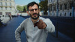 © Krakenimages.com - Hispanic man with beard and glasses stands outdoors on a busy street pointing with a serious expression in an urban setting.