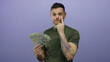 © Krakenimages.com - Young hispanic man with tattoos holding us dollars against a purple background, embodying a modern confident attitude with subtle gestures of thought and contemplation.
