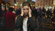 © Krakenimages.com - Woman pressing her temples with both hands as her glasses dangle beside her on a crowded illuminated city street at night; anxiety.