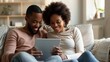 © Antonio  - a diverse couple in their early 30s sitting together on a modern couch, looking at fertility test results on tablet, warm natural lighting, comfortable home setting