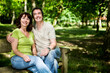 © track5 - A happy mature couple sit on a park bench enjoying the summer in a forest. The man has his arm around the woman in a loving embrace. From a series of images.