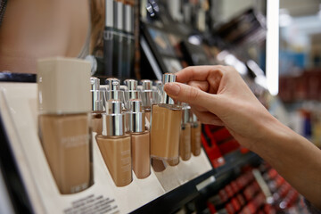 Wall Mural - A woman is reaching for a bottle of foundation on a store shelf
