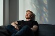 © Gordana - A man enjoys a moment of peace and joy while lounging on a couch illuminated by colorful sunlight reflections