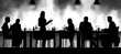 © app - Silhouettes of six people seated and one standing around a long table with various glasses and bottles in a dimly lit room, evoking a social and relaxed atmosphere