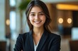 © ali - Young woman with long dark hair wearing a black blazer and white shirt smiling confidently indoors with blurred office background