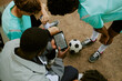 © Seventyfour - Group of teenage boys including Black and Caucasian teammates studying soccer tactics on digital tablet during outdoor practice session, sitting together near soccer ball on field