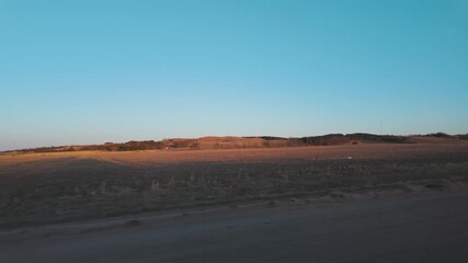 Wall Mural - Golden sunlight touches dry land under a clear blue sky with distant hills on the horizon