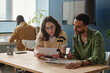 © TrueFrame Collective - Young woman reading document and discussing it with her colleague while they working in team at table at office