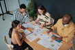 © TrueFrame Collective - High angle view of business people sitting at table examining documents with charts and planning new strategy in team at meeting