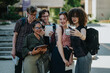 © qunica.com - A diverse group of college students enjoying a moment together outdoors, taking a selfie on a sunny day. The image showcases academic camaraderie, joy, and school environment in a relaxed setting.
