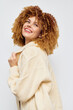 © SHOTPRIME STUDIO - Happy woman with curly hair smiling on a plain white background, wearing a cozy beige cardigan, exuding warmth and joy, perfect for lifestyle and fashion themes