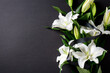 © photoguns - White lilies with black ribbon on black background. Symbolic floral arrangement for funeral, mourning, remembrance, or condolence themes. Elegant and minimalist composition.