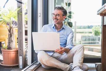 Smiling businessman with laptop sitting on floor at home office
