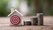 © AndiAzis - Miniature house model with a red symbol and stacks of coins on a wooden representing financial goals and investment planning