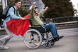 © Westend61 - Person in wheelchair with superhero cape racing in city with companion