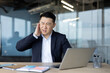 © Tetiana - Asian young businessman sitting at the desk in the office and holding his ear with his hand, feeling severe pain