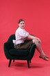© New Africa - Beautiful young woman sitting on armchair against red background