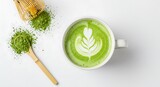 Top view of a hot matcha green tea latte with foam art, powder, and a bamboo whisk on a white table.