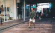 © BullRun - Smiling man in urban plaza with smoothie walks past storefronts, showing active tech lifestyle, modern social fluidity, and digital integration in real-world flow.