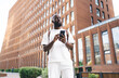 © BullRun - Focused Black man using smartphone while standing downtown, deeply engaged with mobile interface, symbolizing digital multitasking, modern work, and connected city lifestyle.