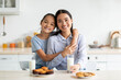 © Prostock-studio - Loving korean mother and her daughter enjoying fresh homemade cookies, drinking milk, sitting at tablet in kitchen interior and smiling at camera, spending time together at home