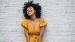 © Johannes - funny happy stylish african american young woman wears yellow trendy sundress with afro hair laughing standing against white brick wall background smiling black hipster woman having fun vertical no l