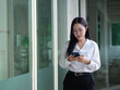 © Oil And Den - An Asian businesswoman or employee stands holding a phone outside.