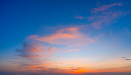 Wall Mural - Radiant pink, orange, and blue clouds are scattered across the sky during the evening. The sun is setting in the distance, casting warm light across the celestial landscape
