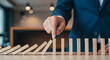© Inspire Shots Hub - Close-up of hand interacting with wooden dominoes, some falling, others standing, symbolizing risk management, planning, and business strategy
