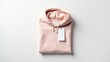 © Leonardo - Sudadera con capucha de color pastel doblada con una etiqueta rectangular visible sobre una superficie blanca, que muestra una disposición plana limpia