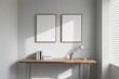 © 张锋 - Two empty poster mockups with wooden frames on a gray wall above a minimalist desk with books and a desk lamp