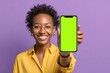© Marina Demidiuk - Cheerful young african american woman showing phone with blank green screen on camera and smiling standing isolated purple background. Man holding smartphone and shows copy space for advertising