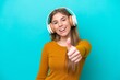 © luismolinero - Young caucasian woman isolated on blue background listening music and with thumb up