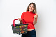 © luismolinero - Young Rumanian woman holding a shopping basket full of food isolated on white background making money gesture