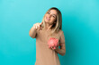 © luismolinero - Young woman holding a piggybank over isolated blue background pointing front with happy expression