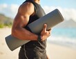 © T.V.Stock - A muscular man holding a yoga mat on the beach, ready for a workout.