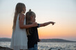 © Milica - Siblings enjoying the sunset by the sea. Two children on the beach rocks, with the little boy pointing towards the horizon while his sister hugs him.