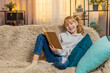 © Andrii Iemelianenko - Young teenager girl rests at home with reading fairy tale book, smiling softly at funny parts. Blonde child kid on sofa suddenly sighs when the plot gets serious, enjoying each page with quiet focus.
