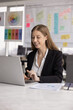 © fizkes - Positive young company CEO woman working at laptop computer in office, typing, smiling, sitting at workplace table, using gadget for professional iNtenret communication. Vertical shot
