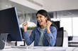 © fizkes - Excited happy young Indian office professional woman in casual celebrating success, triumph, goal achieving, making winner yes fist gesture at computer monitor, laughing, shouting for joy