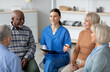 © Prostock-studio - Friendly pretty young woman in blue workwear psychologist having conversation with multiracial group of senior people sitting in circle, psychological support for senior people at nursing home