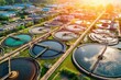 © Cheewynn - Aerial view of a modern wastewater treatment plant with multiple circular tanks and surrounding industrial buildings at sunrise