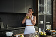 © DragonImages - Middle aged Caucasian woman standing in modern kitchen drinking fresh smoothie from glass, wearing sportswear, surrounded by fruits and blender on countertop, eyes closed enjoying beverage
